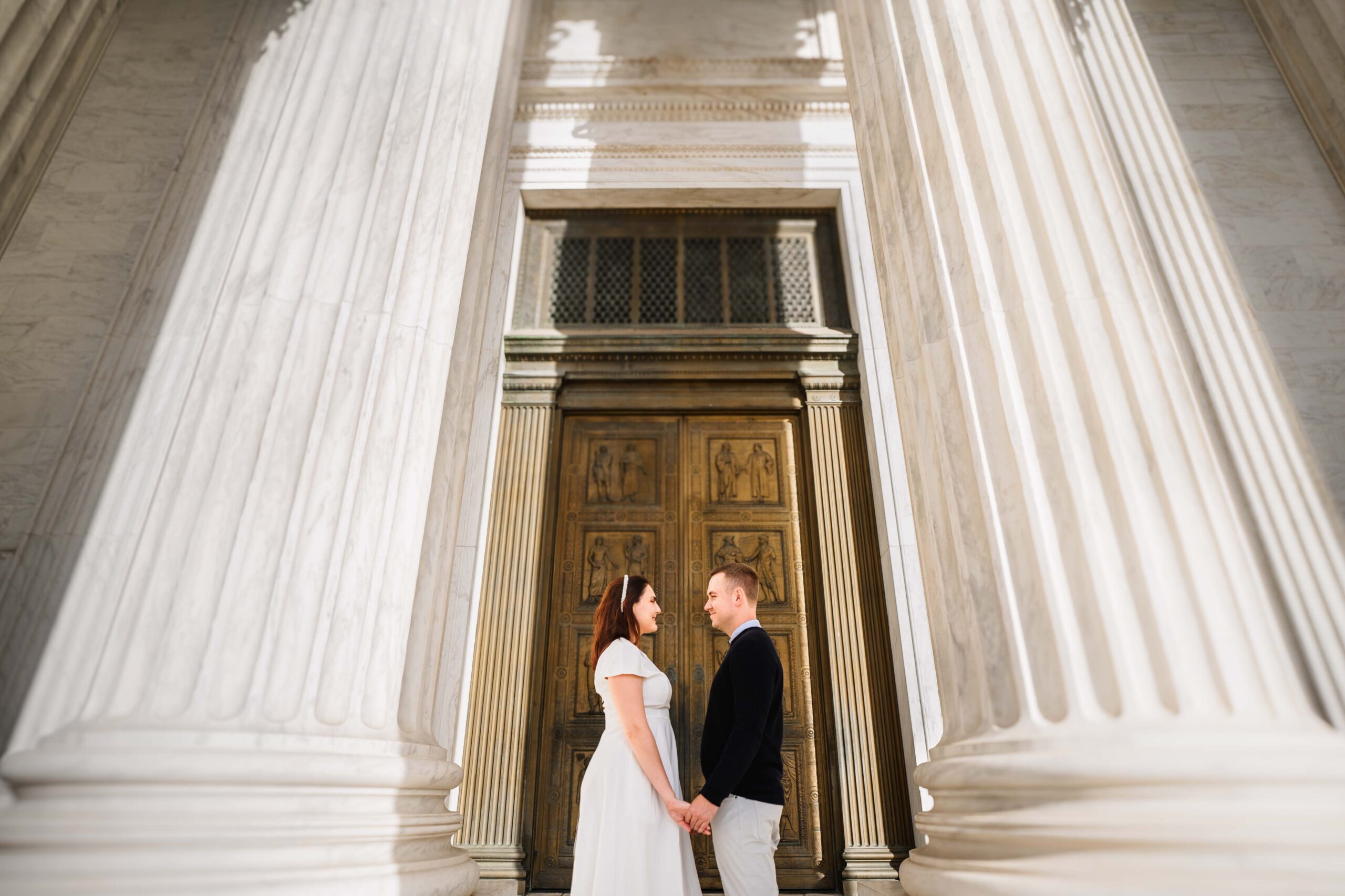 couple hold hand stand in front of a gold door at the supreme court in washington DC